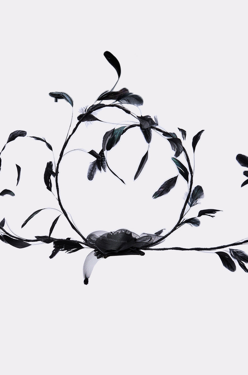 The IN YOUR DREAMS CLIP ON HAT is a dramatic black headpiece with intricate leaf and flower designs on winding branches, shown against a plain white background. 3