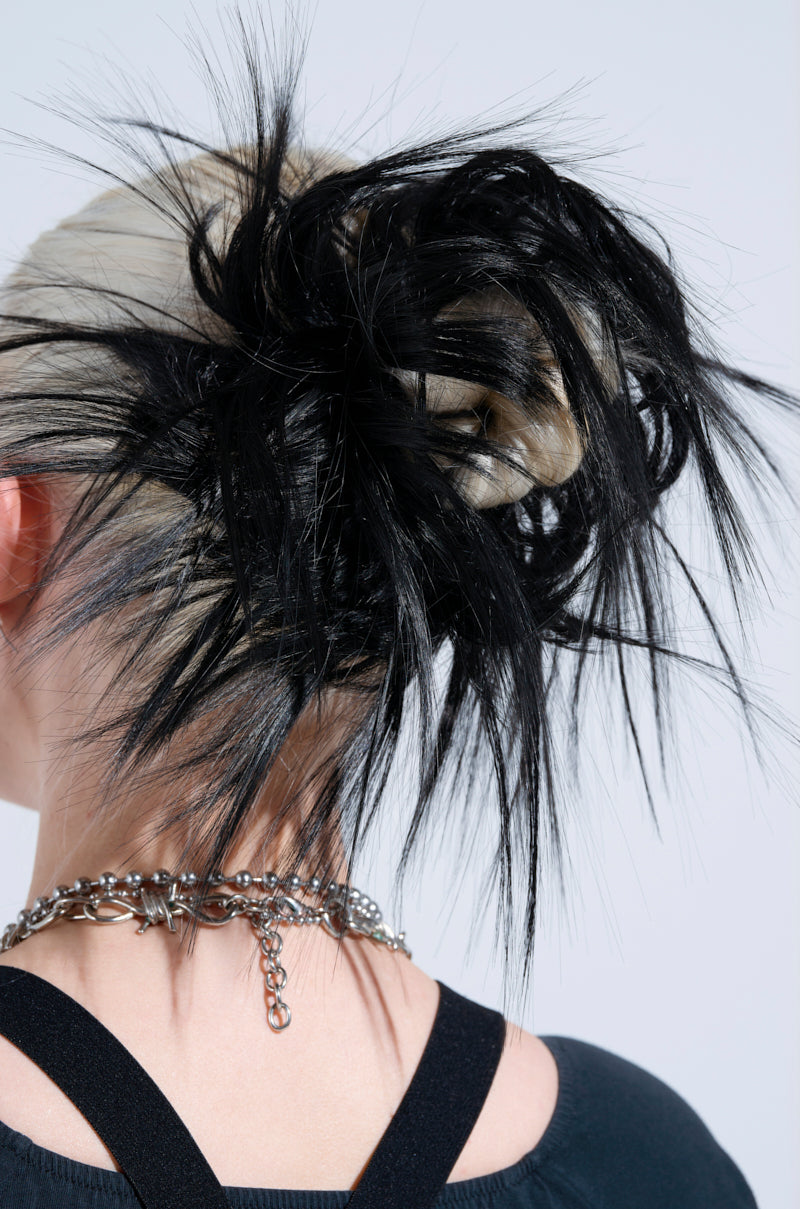 A person with platinum blonde hair styled in a bun is wearing the Spiked Out Hair Piece, adding a punk-meets-glam vibe. Paired with a black top and chunky silver chain necklace, they create an edgy silhouette against a plain light background.