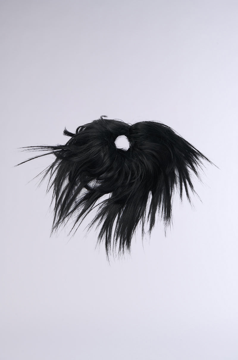 The SPIKED OUT HAIR PIECE features black, shaggy, long uneven strands spreading out in an edgy punk-inspired silhouette against a plain light gray background. 2