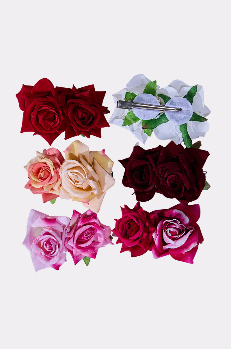 Seven pairs of ROSES ARE RED HAIR CLIPS in vibrant shades—red, white, peach, pink, magenta—are displayed on a light background. One floral clip is flipped to show the secure metal clasp.
