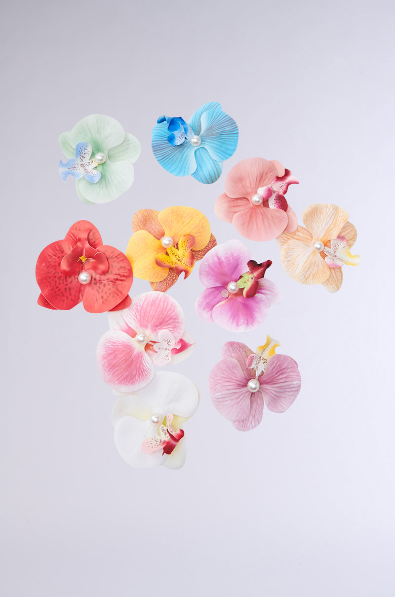 The INTO THE GARDEN HAIR CLIP SET features ten vibrant orchid clips, each with a central pearl, arranged on a light gray background—ideal for adding a colorful tropical accent to any hairstyle.