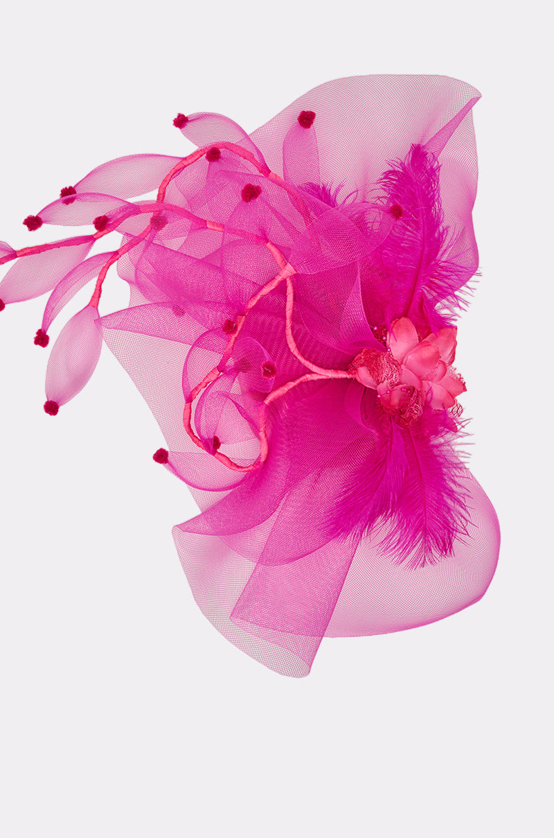 The RIRI HEADPIECE is a vibrant hot pink feather headpiece with sheer mesh, artificial flowers, and looping stems with pom-poms—a stunning floral accessory perfect for festivals, shown against a plain white background. 4