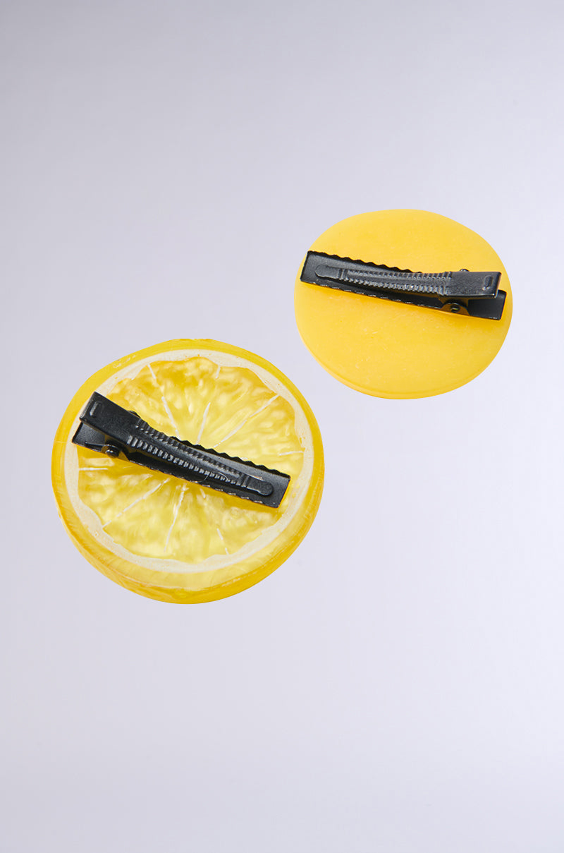 The LIFE GIVES YOU LEMONS HAIR CLIP SET includes two barrette-style clips: one shaped like a lemon slice and the other a solid yellow circle, both with black metal fasteners on a light gray background. 4
