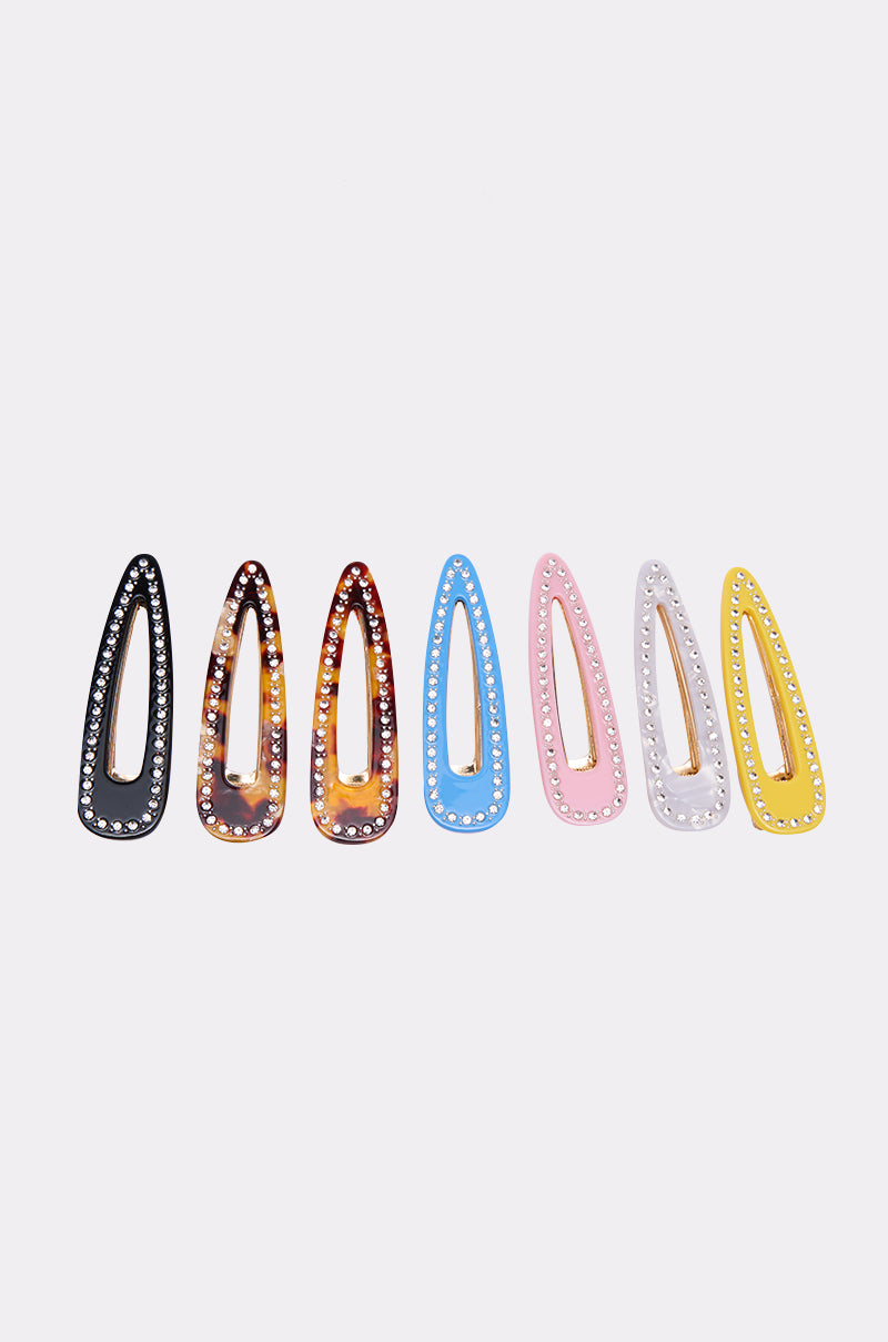 The JUST CLIP IT SET features six barrette hair clips in black, tortoiseshell, blue, pink, white, and yellow, each lined with sparkling rhinestones along the edges and displayed side by side on a white background. 3