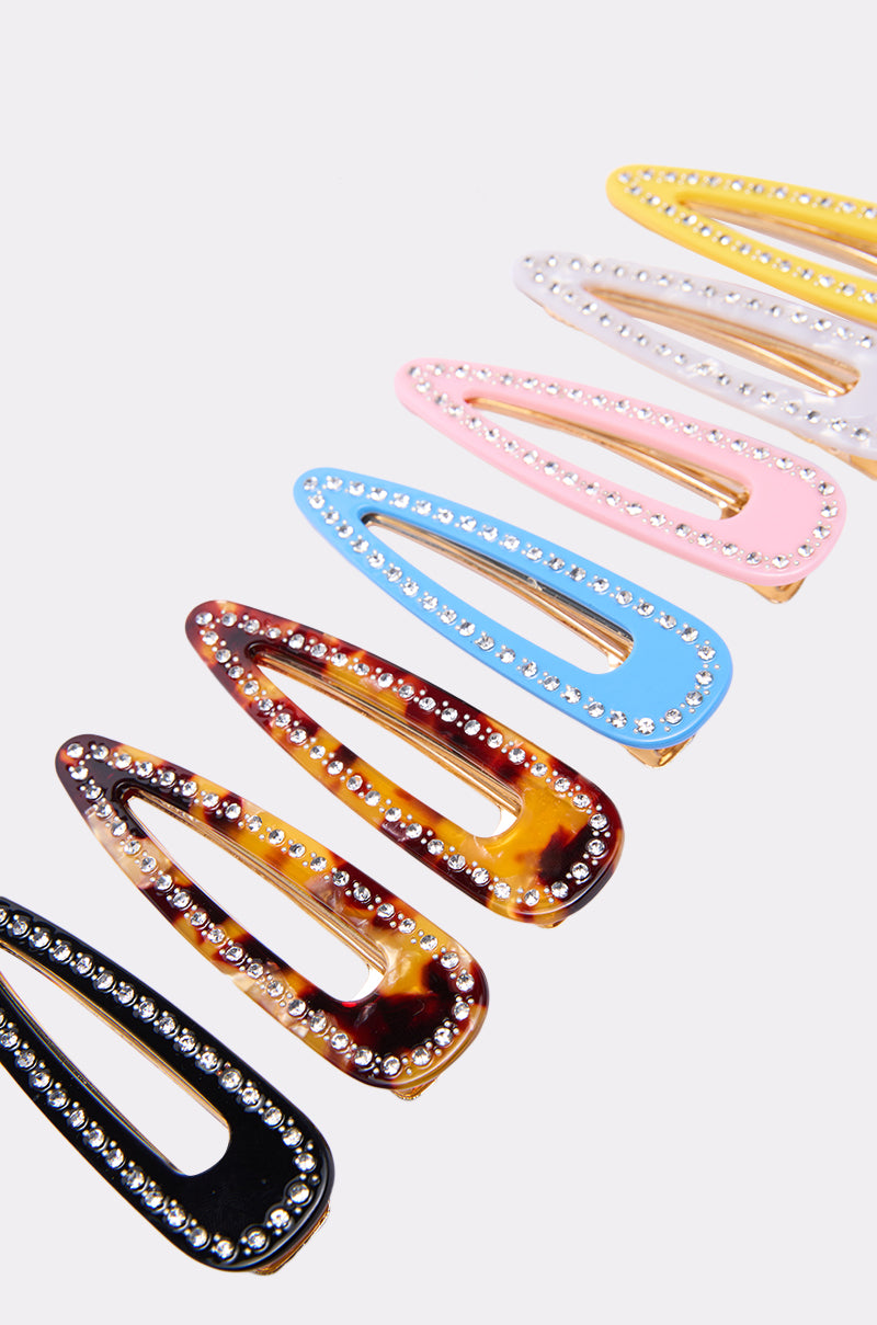 The JUST CLIP IT SET features seven sparkling rhinestone hair clips in black, tortoiseshell, red, blue, pink, cream, and yellow, arranged diagonally on a white background. 0