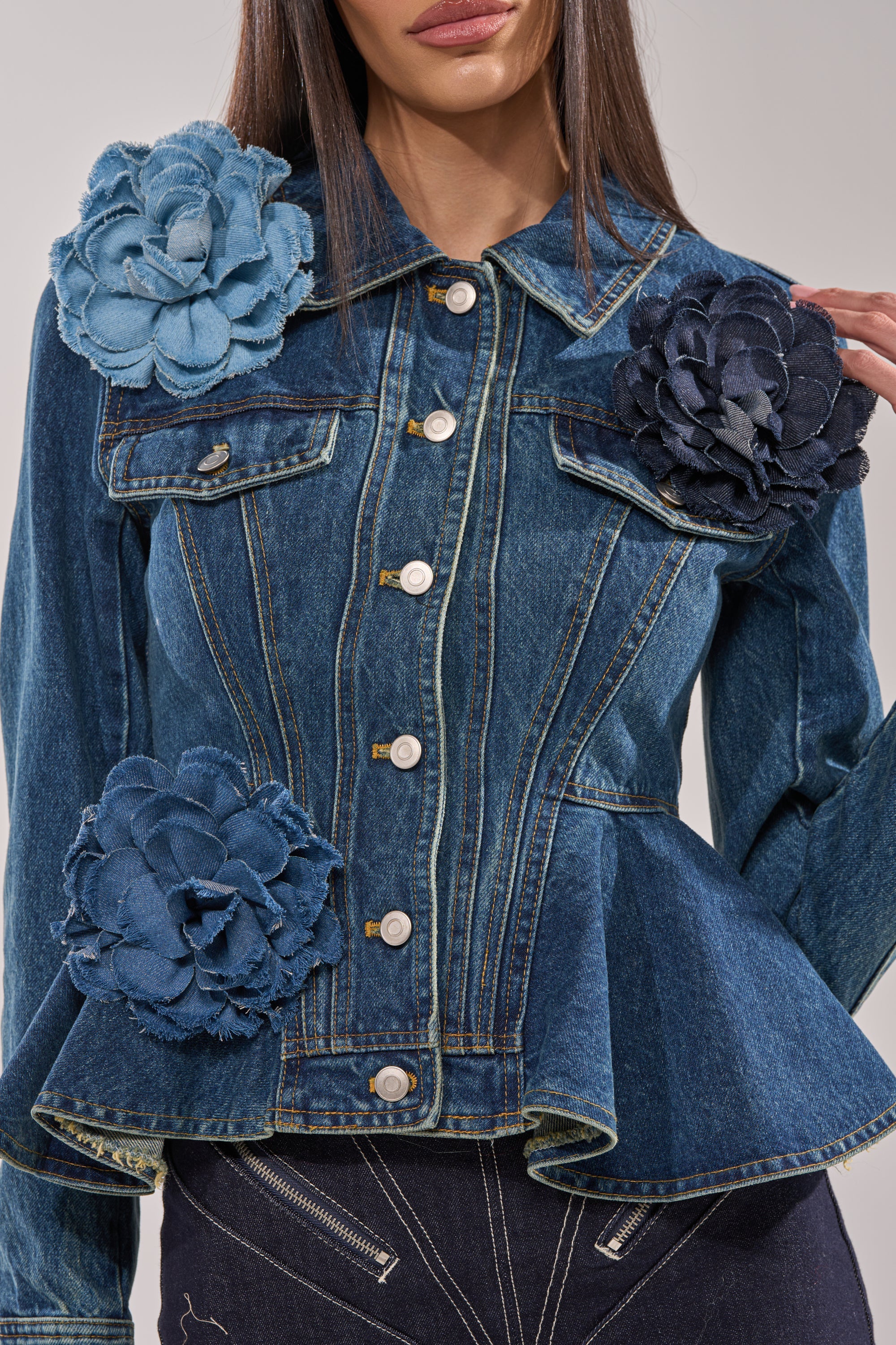 A woman pairs dark denim pants with a fitted jacket adorned by the DENIM ERA BROOCH—a bold blue and black fabric flower appliqué on the shoulder and waist—showcasing stylish streetwear with an edgy, trendy vibe. Her face is partially visible. 4