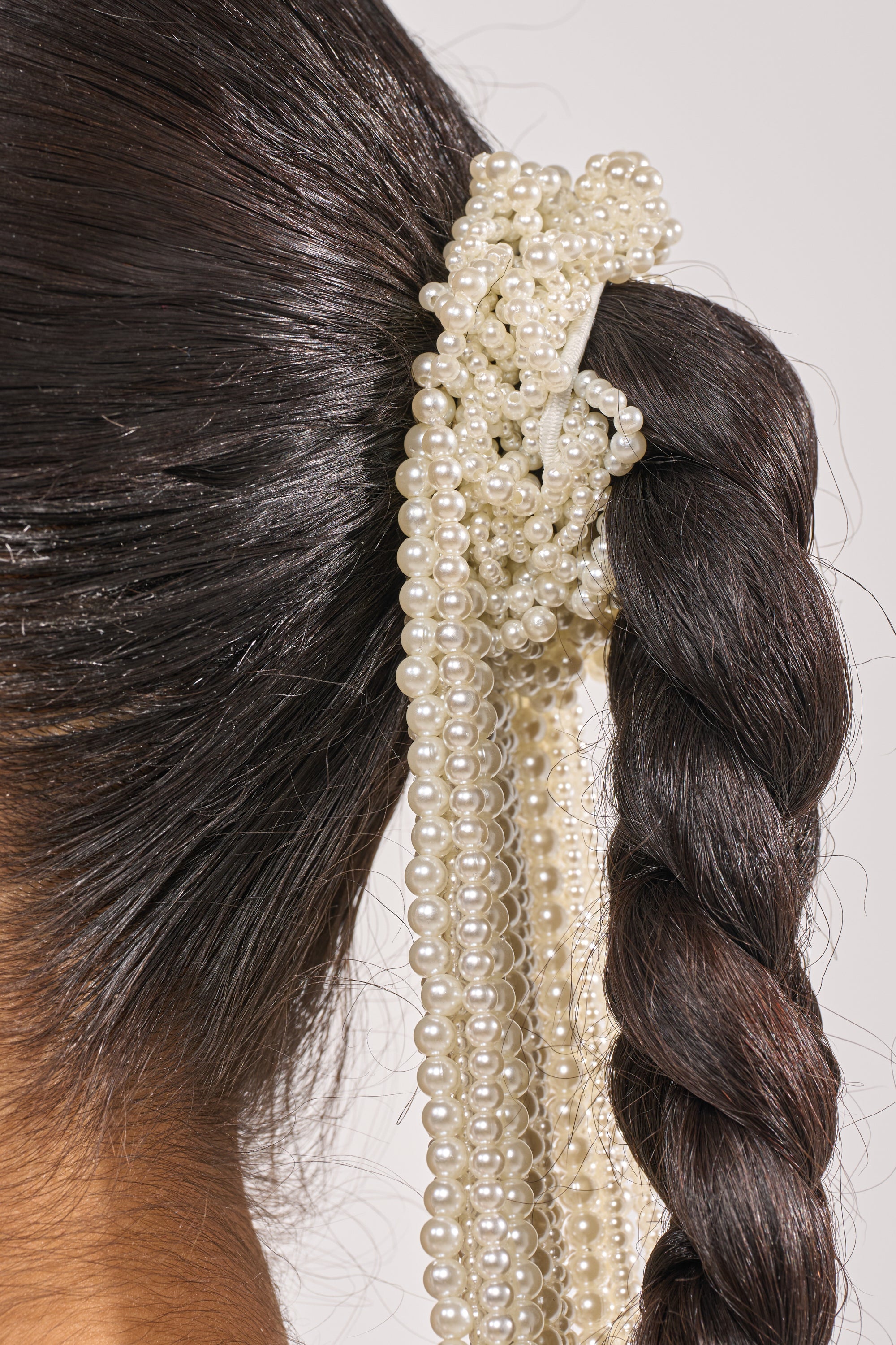 Close-up of a woman's dark braid styled with the PURE VIBES PEARL HAIR ACCESSORY, featuring multiple strands of white pearls wrapped around the base and elegantly cascading down the braid. 2