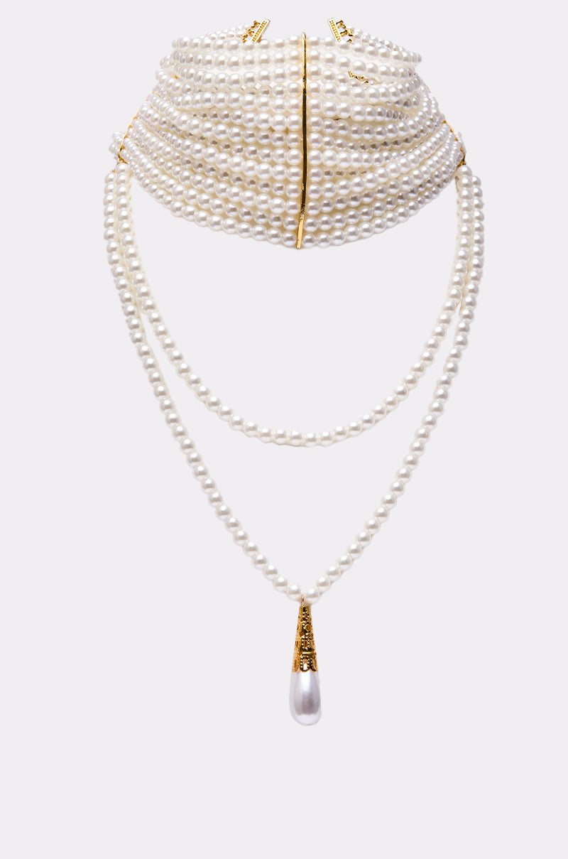 The VERSAILLES NECKLACE is a layered faux pearl choker with multiple strands and a long, drop-shaped pearl pendant in a gold-capped setting—an eye-catching accessory shown on a light gray background.