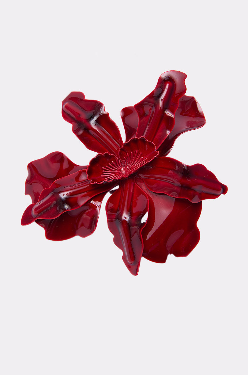 The WATCH ME RING features a shiny, deep red, flower-shaped design with layered, wavy petals and a detailed center—making it a bold accessory that stands out against a plain white background.