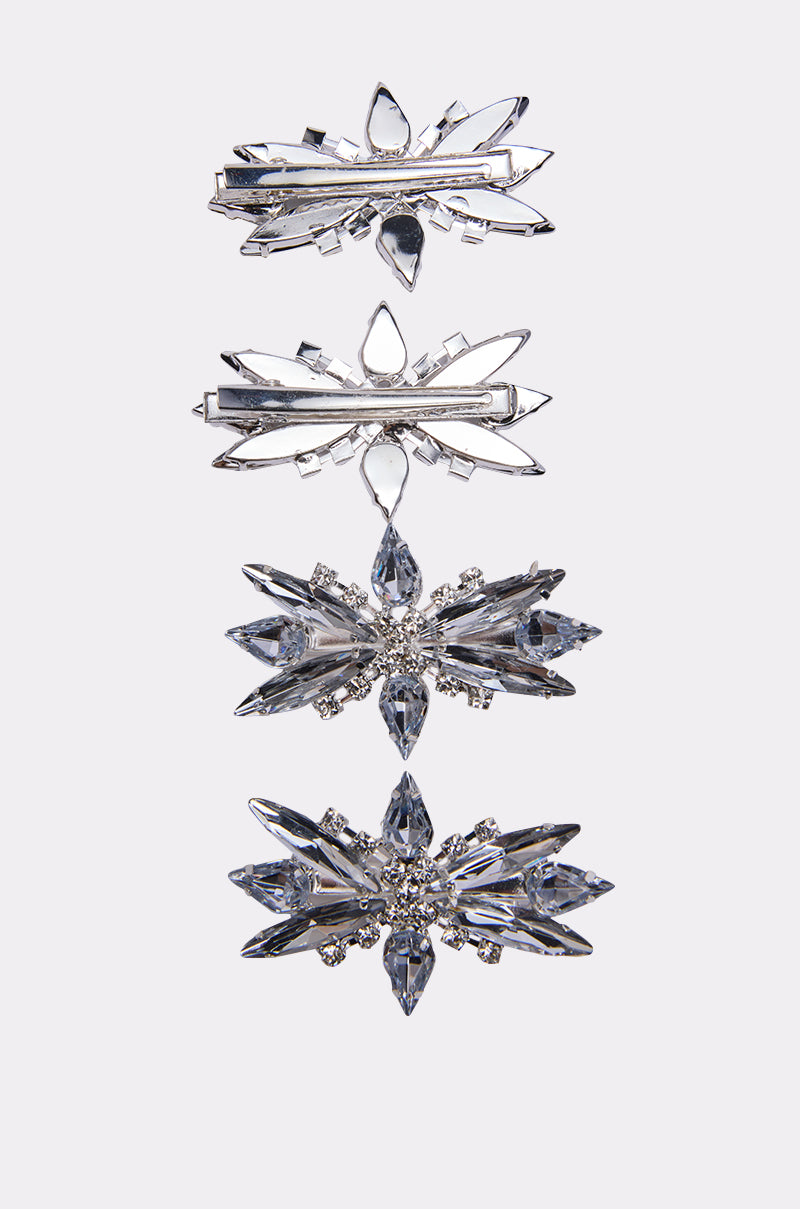 The DECO RHINESTONE 4 PK CLIPS features four silver hair clips with crystal rhinestones in snowflake and starburst shapes, arranged vertically on a white background—perfect for adding sparkle and glamour to any hairstyle.