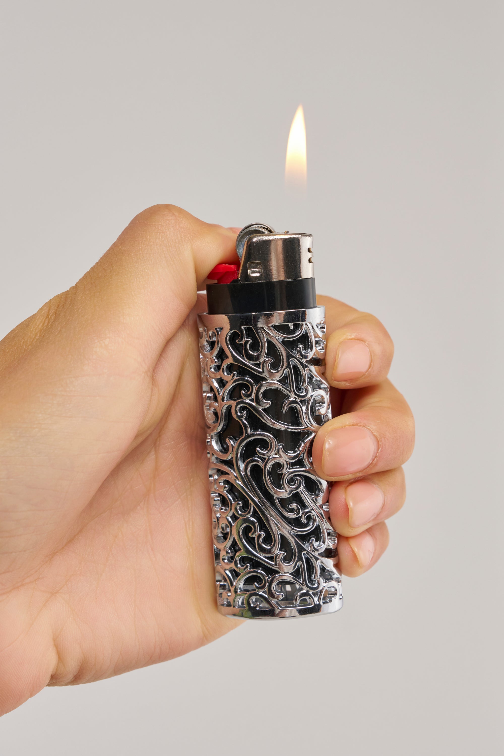 A hand holds a lit lighter adorned with the SILVER ERA LIGHTER CASE, its ornate engraved pattern gleaming against a plain background.