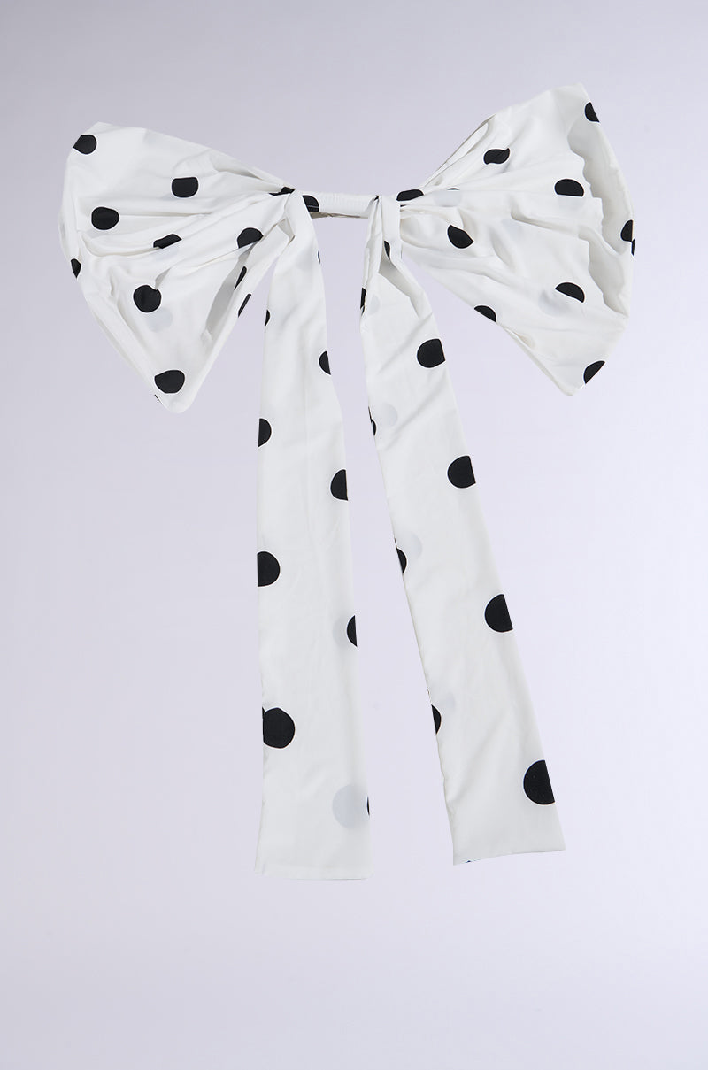 The POLKA DOT IT HAIR BOW is a large white hair accessory with black polka dots, oversized at the center, featuring two long wide ribbons that cascade elegantly against a simple background.
