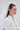 A woman with long brown hair wears the TO THE EXTREME HAIR BOW and a white veil. She pairs this with silver hoop earrings and a rhinestone-detailed white shirt, gazing to the side with a neutral expression.