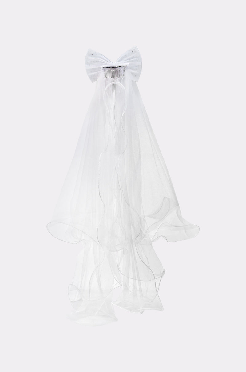 The TO THE EXTREME HAIR BOW is a white bridal veil featuring a dramatic, oversized bow at the top, crafted from sheer, lightweight fabric that flows gracefully in layered cascades against a plain background.