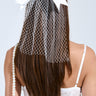 The image features a woman with long brown hair adorned by the POSE NETTED HAIR BOW, its satin material draping gracefully over her head. She wears a white lace spaghetti strap outfit and elegantly holds a pearl strap.