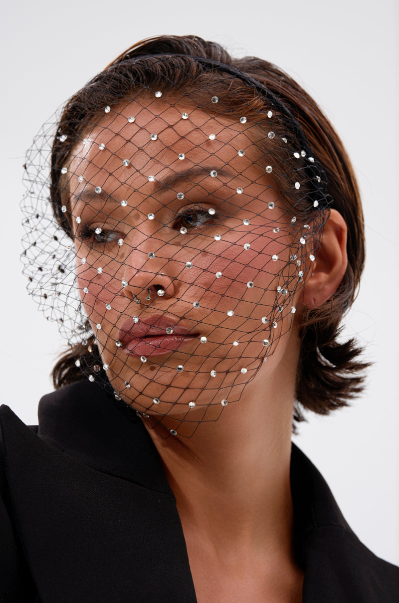 A woman with short brown hair wears a black blazer and netted veil with white beads, facing slightly to the side against a plain light background. Her look is elevated by the HAILEY BLING HEADBAND. 2