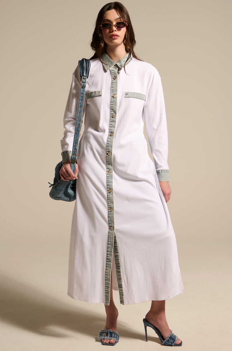 A woman wearing the LEILA OVERSIZED WHITE MULTI BUTTON UP with light-wash denim trim, sunglasses, a denim shoulder bag, and blue open-toe heels stands against a beige background.