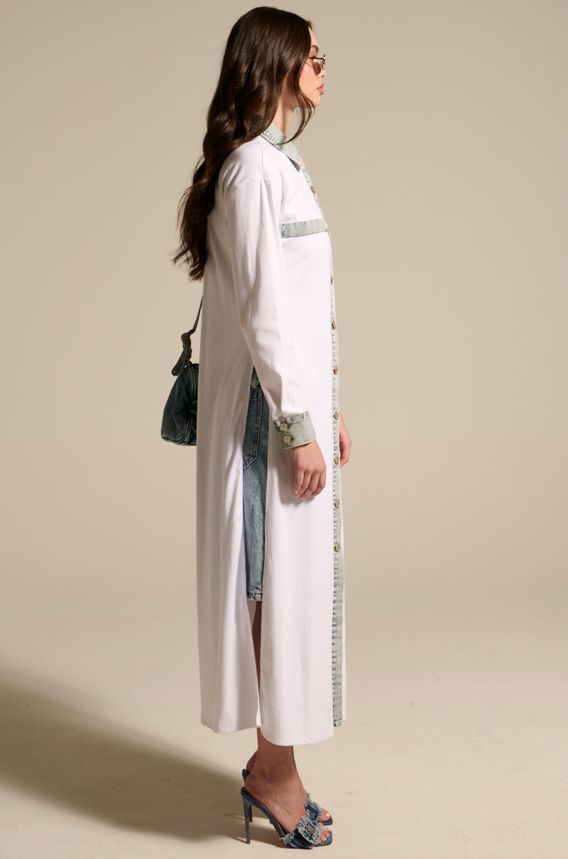 Woman in profile wearing the LEILA OVERSIZED WHITE MULTI BUTTON UP shirt dress with light-washed denim trim, blue heeled sandals, sunglasses, and a small blue handbag against a plain neutral background.