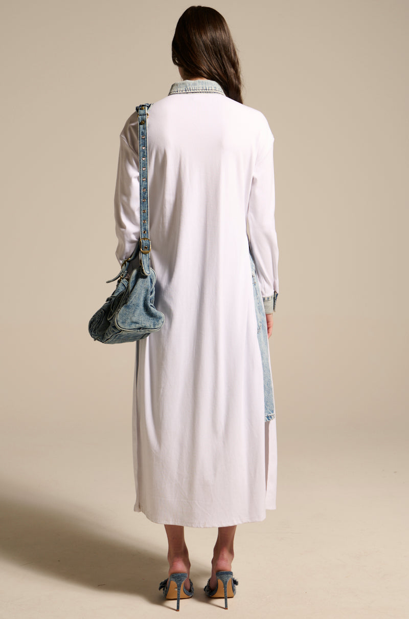 A woman faces away, wearing the LEILA OVERSIZED WHITE MULTI BUTTON UP, blue heeled sandals, and carrying a large denim bag. Her loose brown hair is set against a plain beige background.