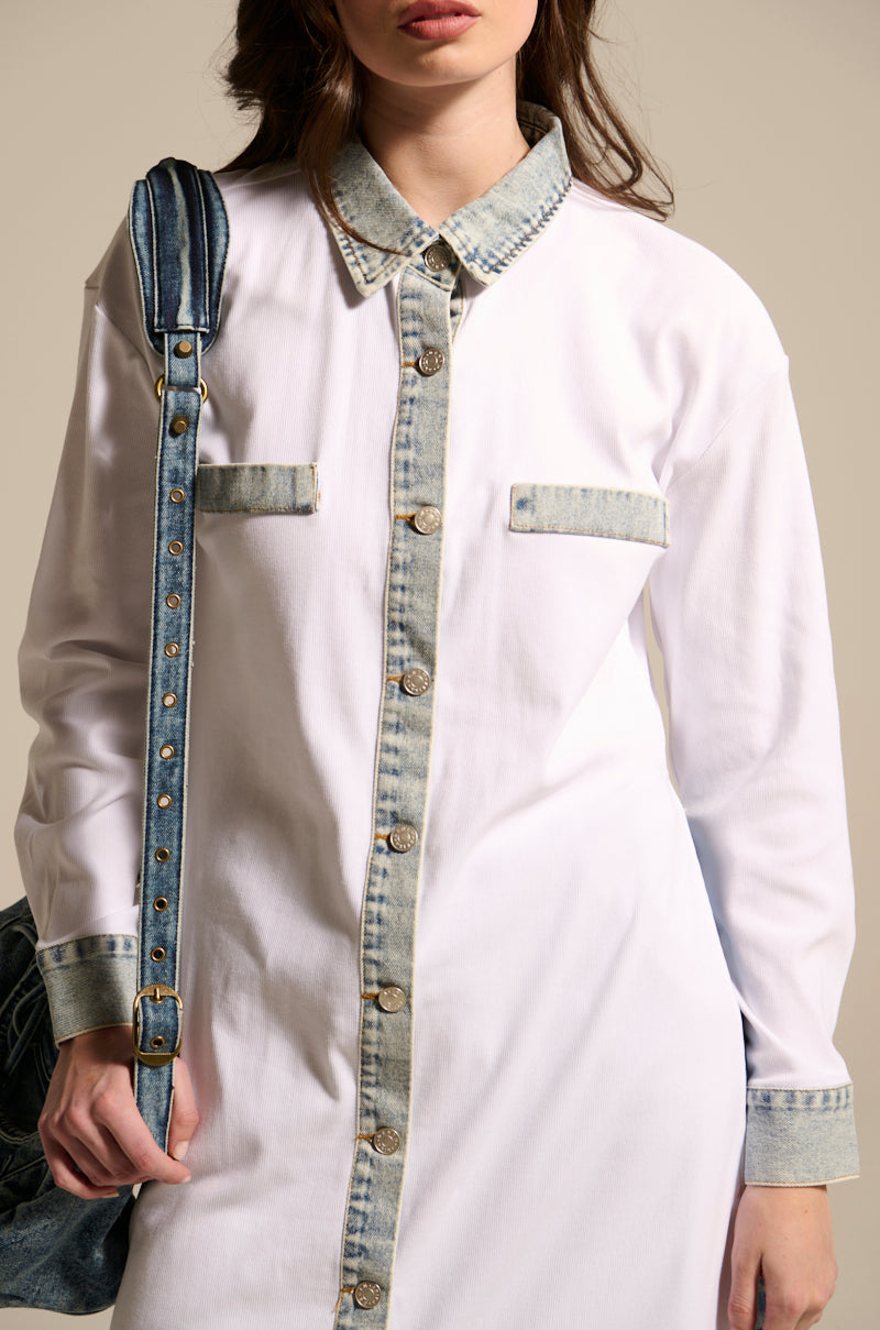 A woman wears the LEILA OVERSIZED WHITE MULTI BUTTON UP, featuring light-washed denim trim on the collar, cuffs, pocket flaps, and button placket. She carries a denim bag over her shoulder while her face is partially out of frame.