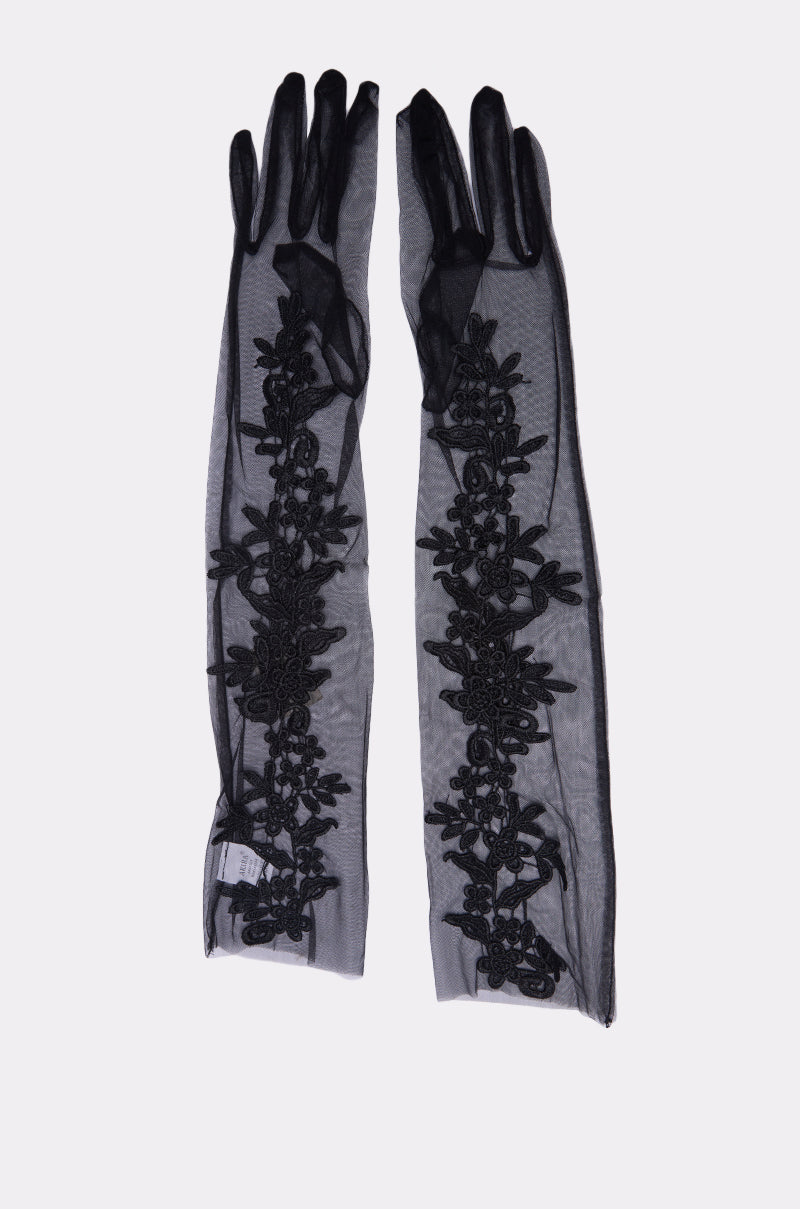 The FLORA MESH GLOVE IN BLACK features long, sheer black mesh gloves adorned with delicate floral lace embroidery along their length, showcased on a simple light background.