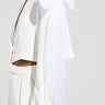A person dressed in a chic TRULY YOURS BOW BROOCH SET, featuring an elegant white outfit adorned with a prominent bow brooch on the shoulder and feathered cuffs on the sleeves. The ensemble includes a cropped blazer and high-waisted pants, beautifully enhanced by delicate pearl beading against a plain light-colored background.