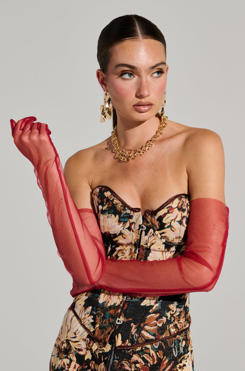A woman stands against a plain background, wearing a floral-patterned strapless top and BURGUNDY MESH GLOVES that extend to an arm-length silhouette. She accessorizes with a chunky gold chain necklace and large gold earrings. Her hair is pulled back in a sleek style, and she gazes to the side with a confident expression. 0
