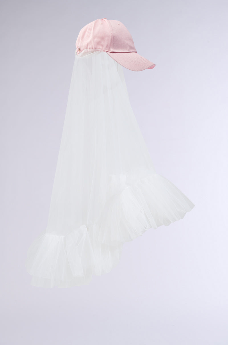 Discover the CITY NIGHTS VEILED HAT by AKIRA Label: a pink baseball cap with a long white tulle veil, creating a stunning contrast against the pastel cap. 4