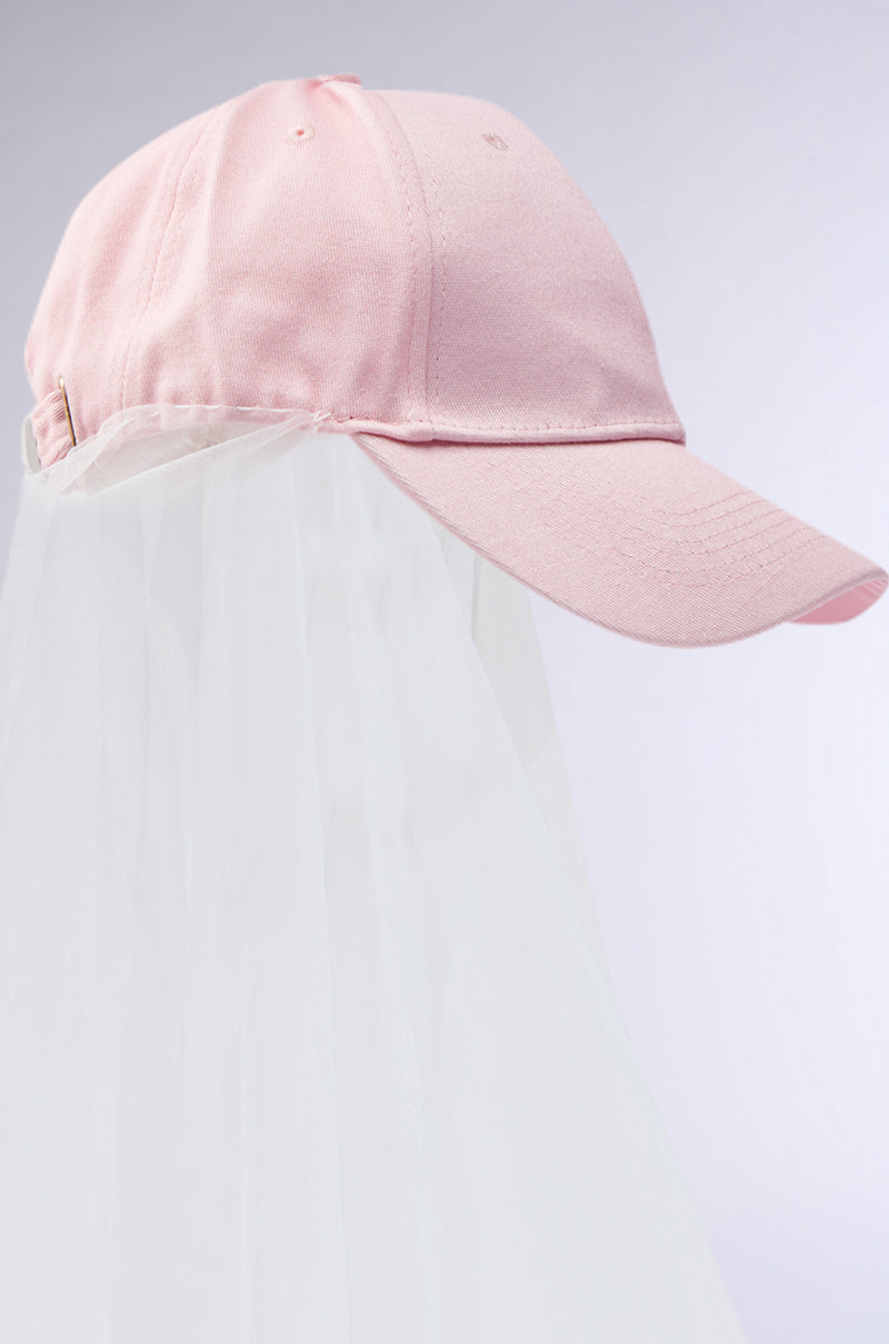 The CITY NIGHTS VEILED HAT from the AKIRA Label is a pink baseball cap featuring a sheer white veil cascading from the back, set against a light gray background. It uniquely blends sporty and chic styles. 5