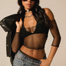 A person exudes confidence, styled in oversized sunglasses, a fishnet mesh top layered with the SIMPLICITY BOLERO AND BRA SET, denim shorts, and a statement necklace. They've draped a black jacket over one shoulder, capturing the perfect festival look against a neutral backdrop.