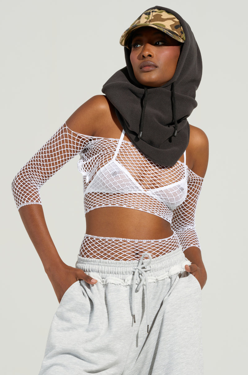 Wearing the LETS RAGE BOLERO AND BRA SET, a person poses confidently, showcasing this edgy festival ensemble with a white mesh top and bralette. The look is completed by pairing it with a camouflage cap, dark hood, and light gray sweatpants against a plain background, emphasizing its fashion-forward appeal.