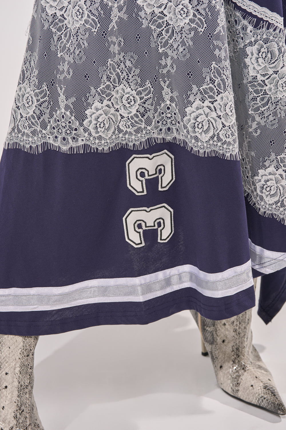 Someone is wearing the BOX SUITE LACE JERSEY MAXI DRESS in navy blue with a white lace overlay and "33" stitched near the hem, styled with pointed-toe patterned cowboy boots. 7