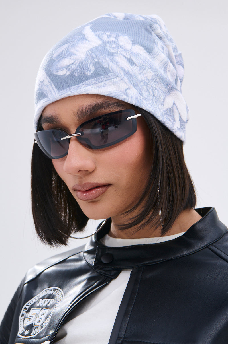 A person with straight black hair wears the CITY OF ANGELS PRINTED BEANIE, slim black sunglasses, and a black faux leather jacket featuring a round white shoulder patch, set against a plain light background. 1