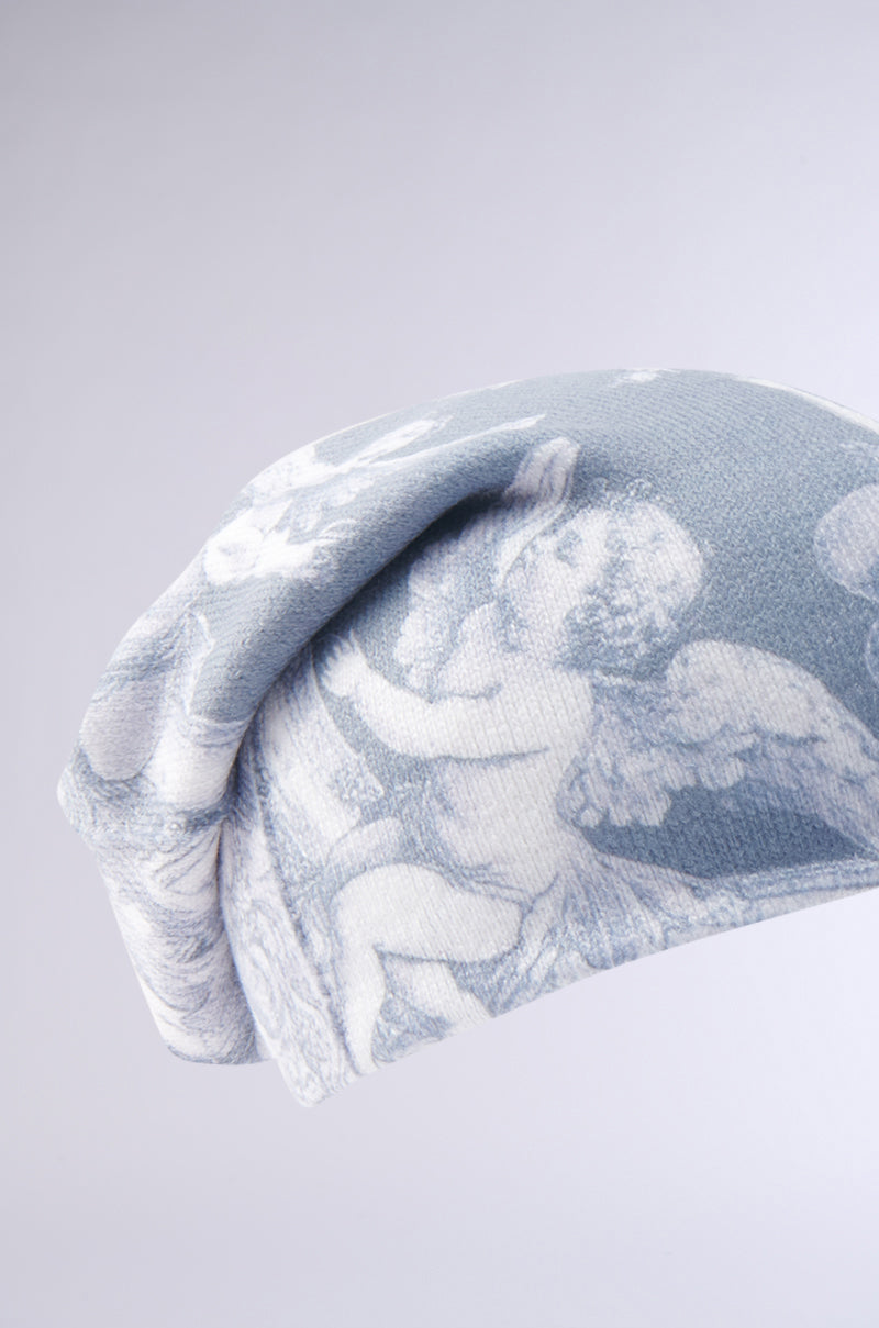 The CITY OF ANGELS PRINTED BEANIE is a light blue beanie with a white vintage cherub and angel print, made from stretchy fabric and shown on a plain pale gray background. 5