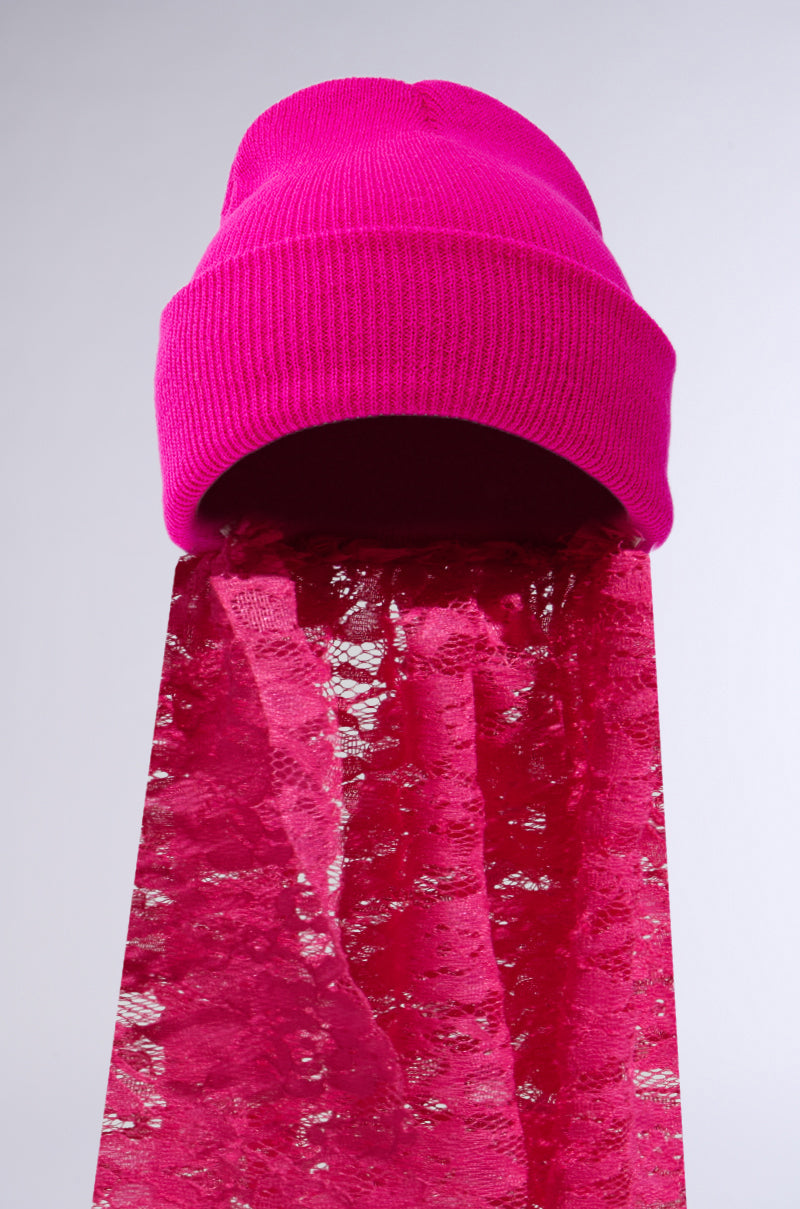 The IN THE CUT LACE VEIL BEANIE features a hot pink beanie with a semi-transparent lace veil, standing upright against a plain white background. The cascading lace creates an eye-catching contrast with the smooth knit texture of the beanie. 4