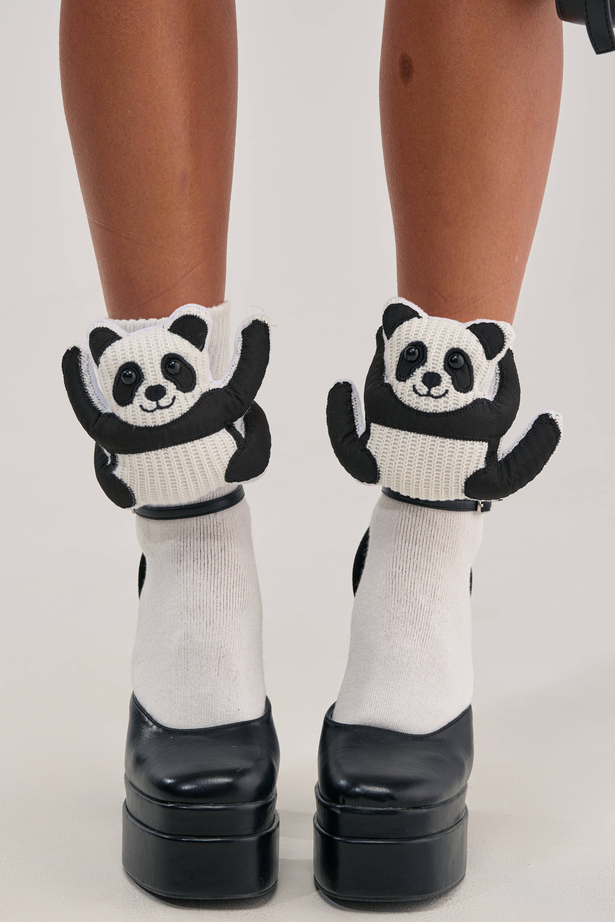 A person wears TOO CUTE PANDA SOCKS, featuring plush panda faces and arms that hug the ankles, paired with black platform shoes for an adorable novelty look.