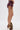 A person stands sideways in HOT DAMN FAUX LEATHER SHORT WITH LACE UP SIDE in burgundy, styled with beige fur-accented high heels. Tattoos show on their thigh and lower leg against a plain white background.