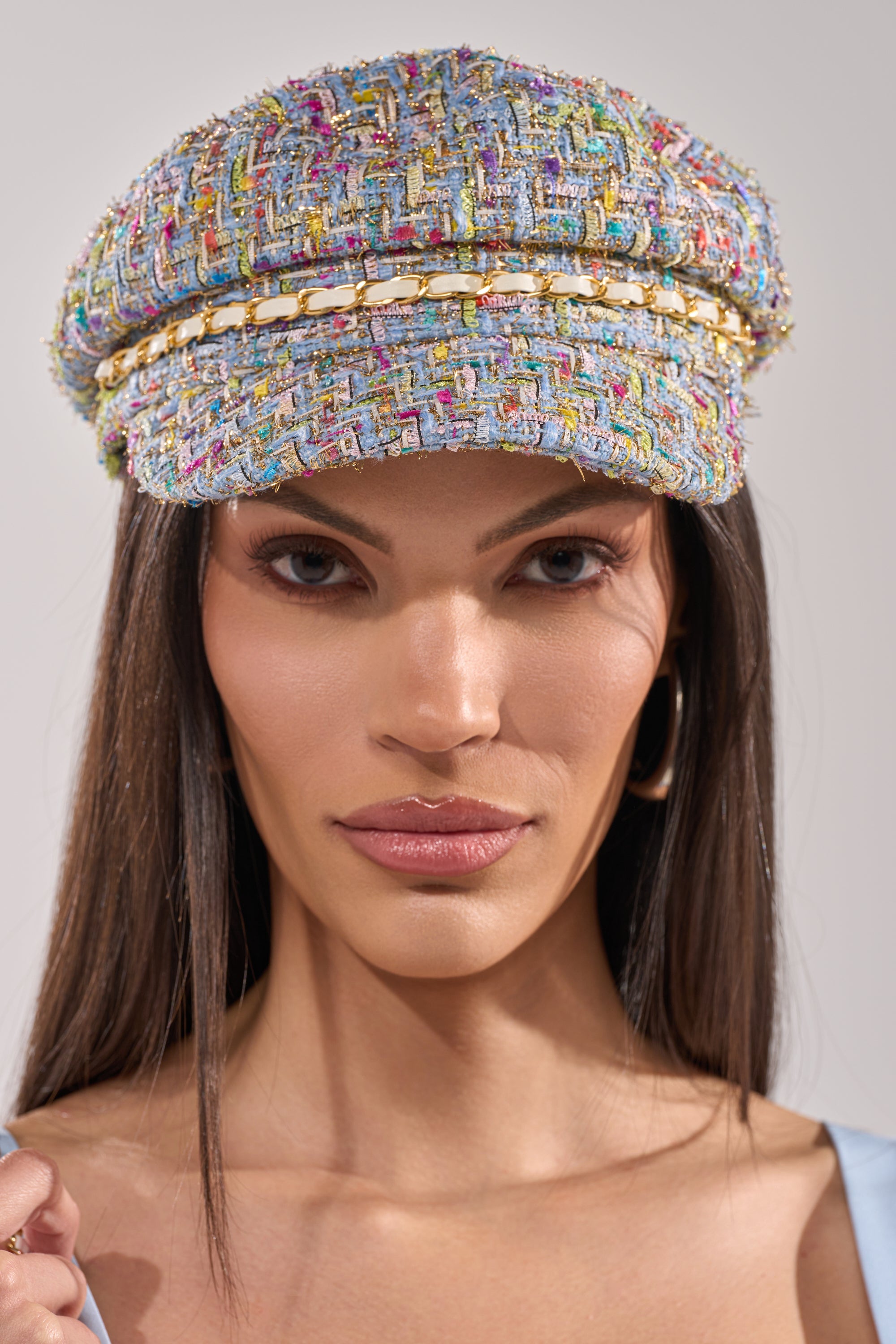 A person with straight brown hair wears the I HAVE CLASS TWEED BRIM HAT featuring a multicolor tweed design and gold chain trim, along with hoop earrings, looking directly at the camera with a neutral expression. 1