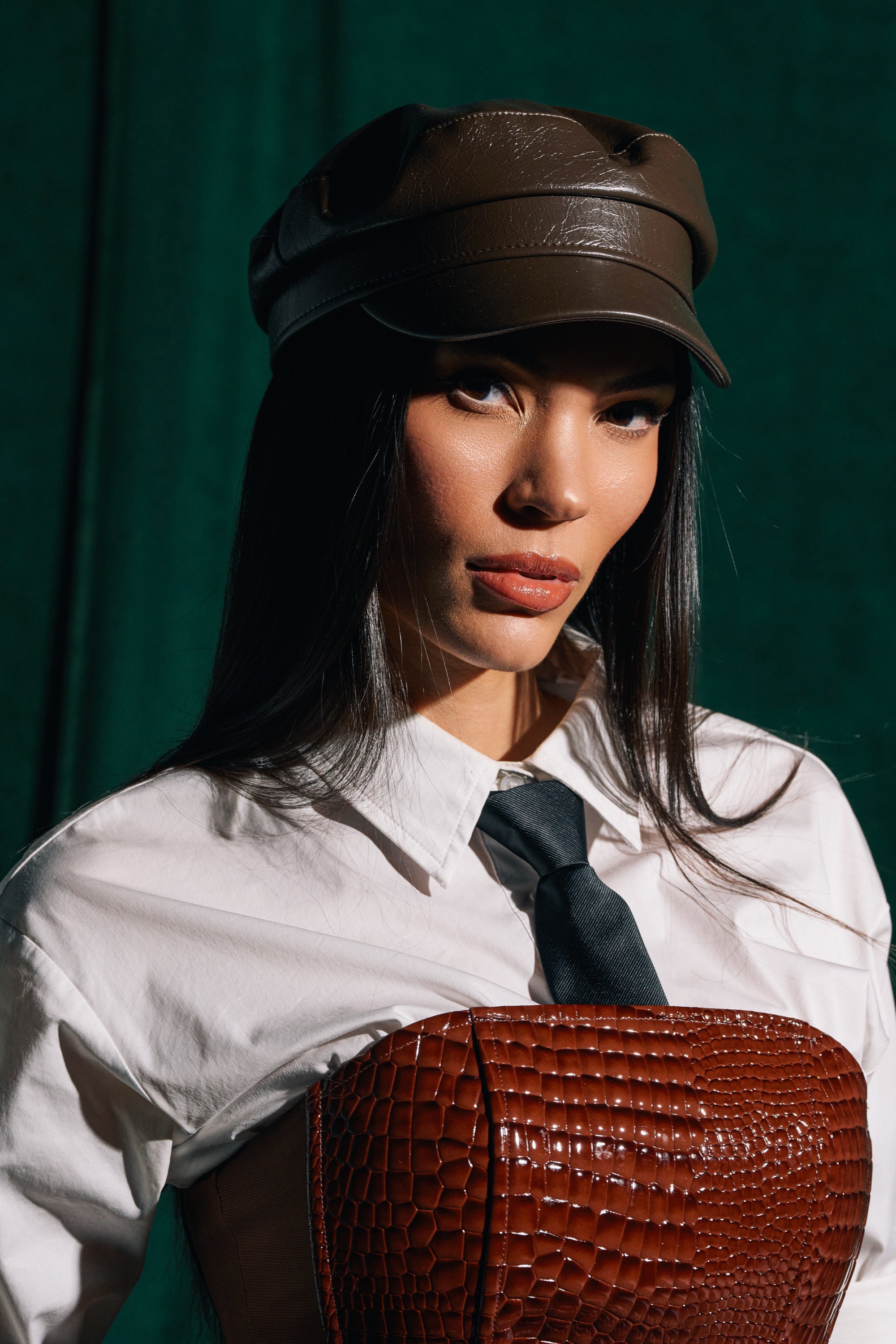 A woman wearing the LIKE BUTTER PU BRIM HAT in brown, a white collared shirt, black tie, and brown textured corset stands against a green background, looking confidently at the camera. 0