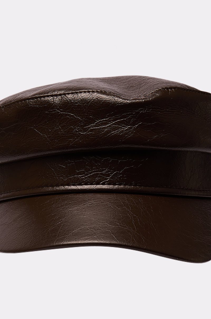 A close-up of the LIKE BUTTER PU BRIM HAT, a shiny dark brown faux leather baker boy hat with a short brim, set against a plain light background. 4
