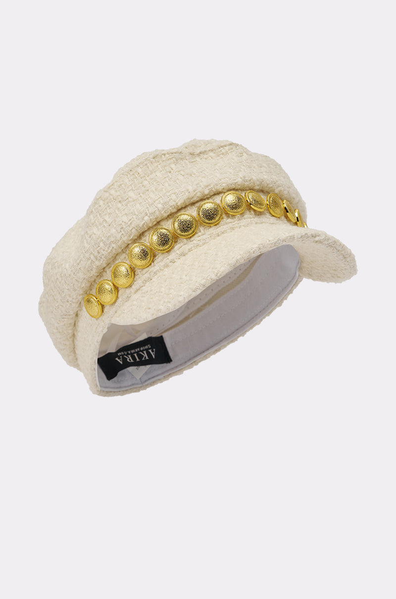 The IN MALLORCA TWEED BRIM HAT is a cream-colored, textured newsboy cap with a short brim, gold coin trim, and round gold buttons for chic street style. The inner label reads "ATIKA PARIS. 4