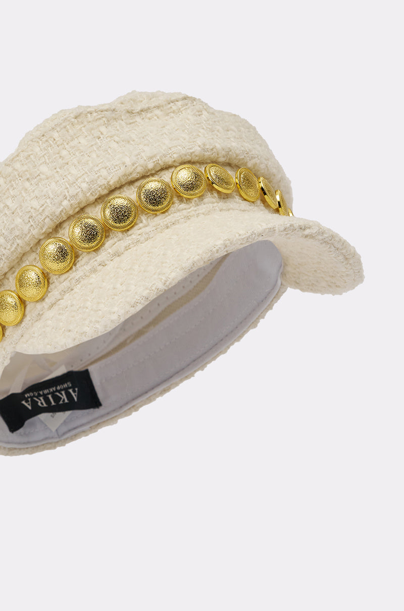 The IN MALLORCA TWEED BRIM HAT is a chic ivory newsboy cap featuring a short brim and gold coin trim above the brim. The "AKIRA" label is inside, and the textured hat is displayed on a plain white background. 6