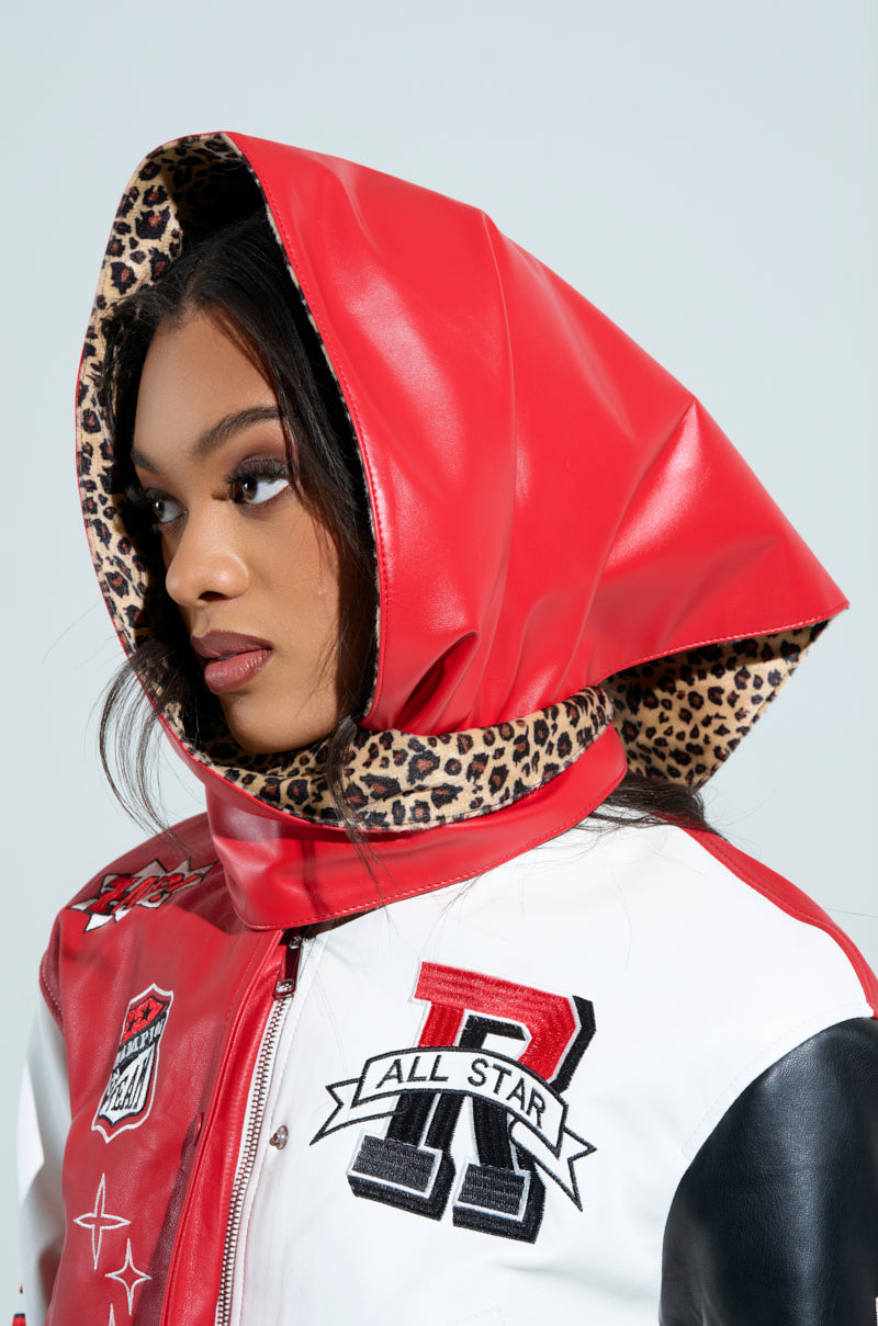 A person wearing a bright red hooded jacket with leopard print lining and a matching RAWR PU HEADSCARF. The jacket displays various patches, including an "R" and "All Star." They look to the side, highlighting their striking profile.
