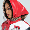 A person wearing a bright red hooded jacket with leopard print lining and a matching RAWR PU HEADSCARF. The jacket displays various patches, including an "R" and "All Star." They look to the side, highlighting their striking profile.