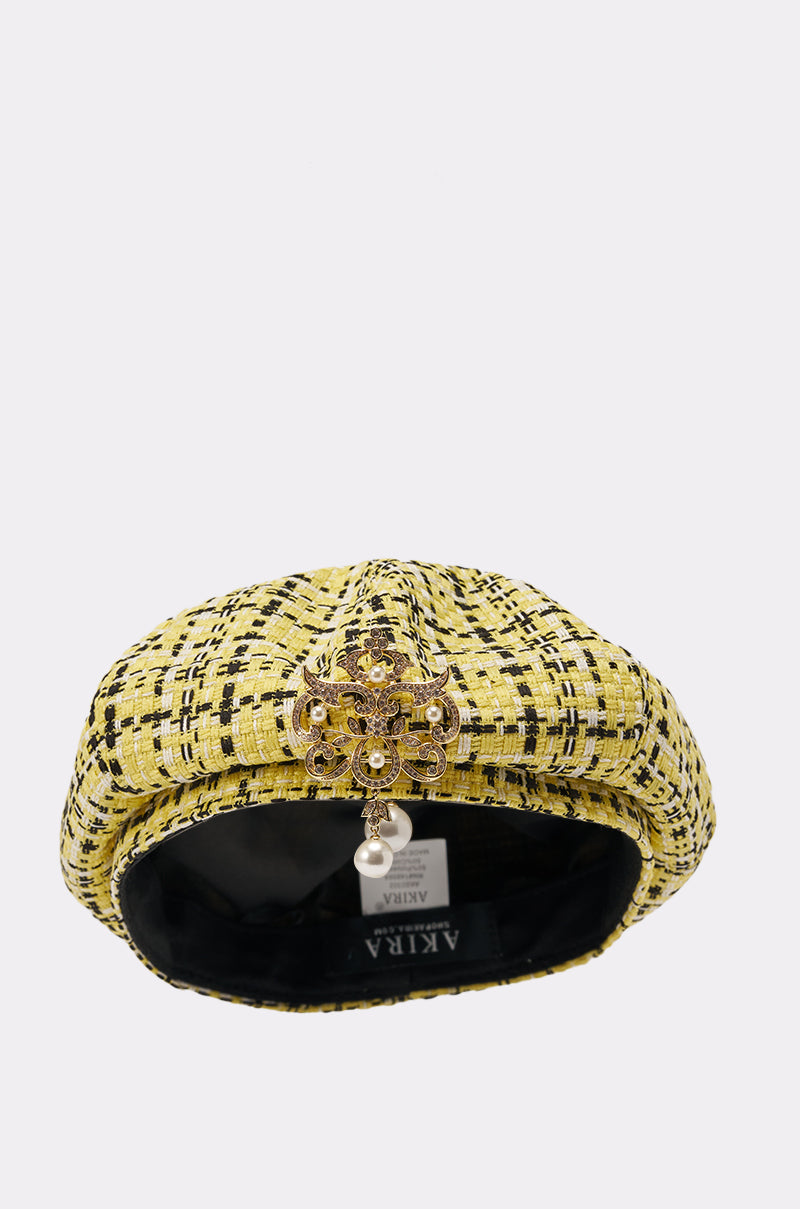 The MIA TWEED BERET, Parisian-inspired in yellow tweed with a gold and pearl brooch on the front, is shown on a white background. The black interior lining and brand tag are visible. 1