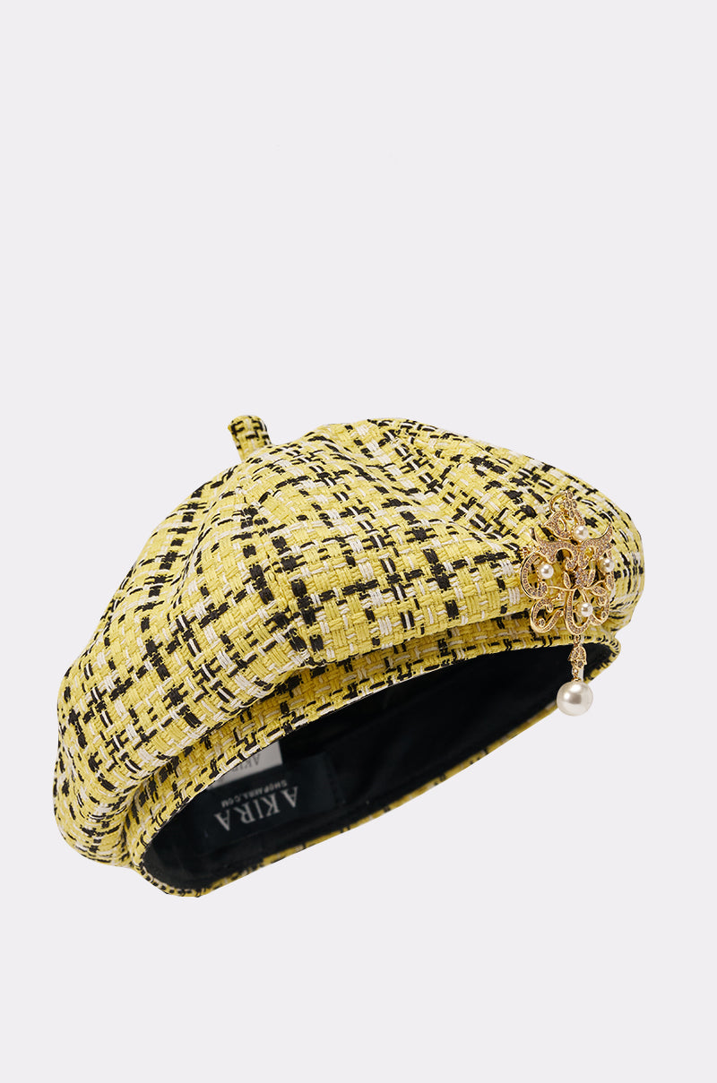 The MIA TWEED BERET is a Parisian-inspired yellow tweed beret with black and white accents, adorned with a gold brooch featuring a pearl drop on the side. 4