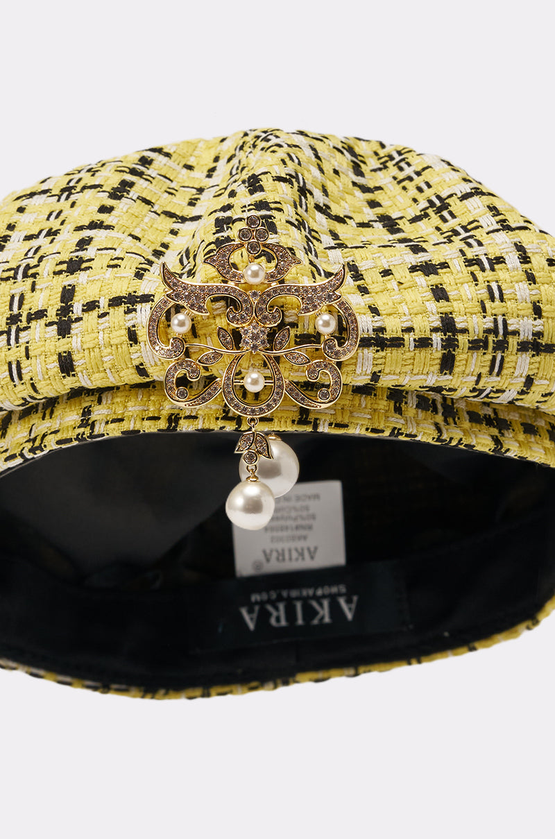 The MIA TWEED BERET is a Parisian-inspired yellow tweed beret with a decorative gold brooch and pearl accents on the front. The inside label reads "AKIRA. 6