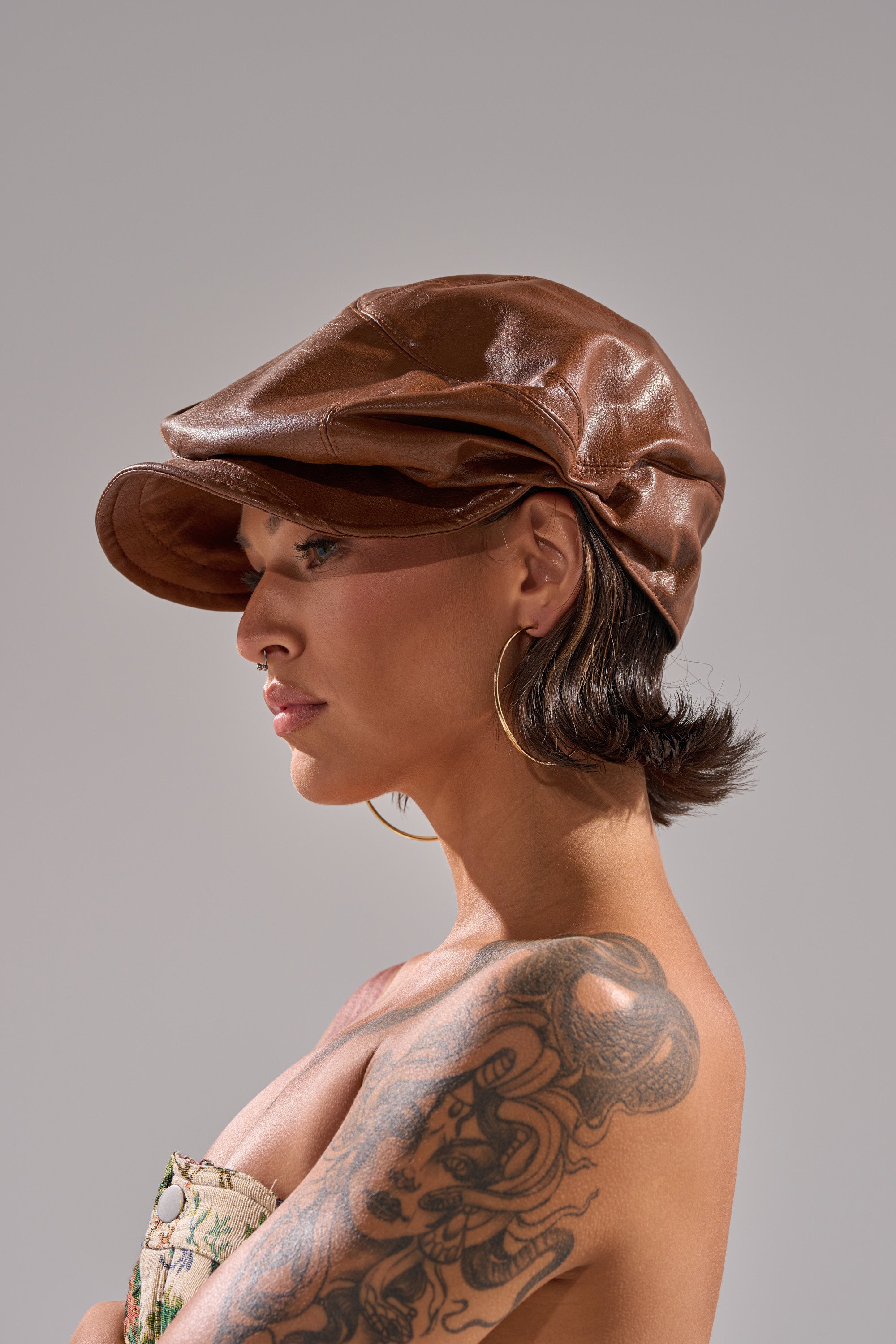 A person with short dark hair wearing the PULL IT OFF HAT, large hoop earrings, and a strapless top shows a detailed shoulder tattoo while posing in profile against a plain gray background. 3