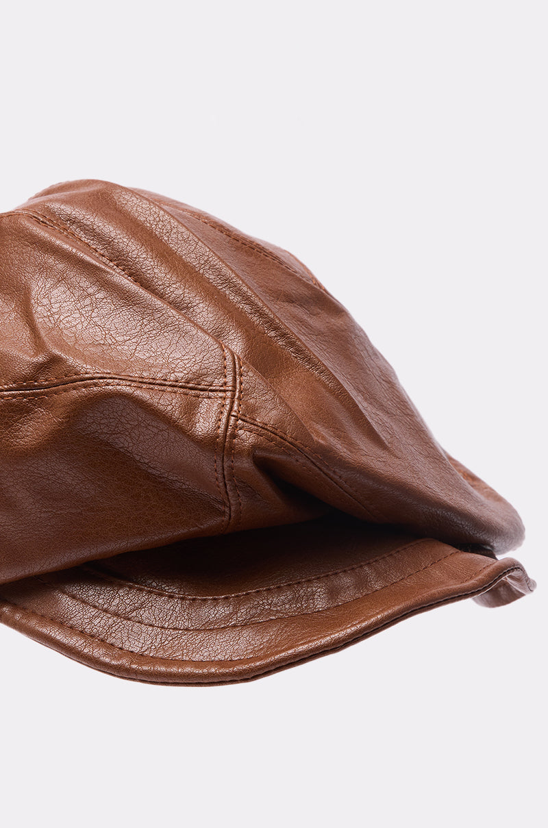 A close-up of the PULL IT OFF HAT by AKIRA Label, a faux leather newsboy cap with visible stitching, set against a plain white background.
