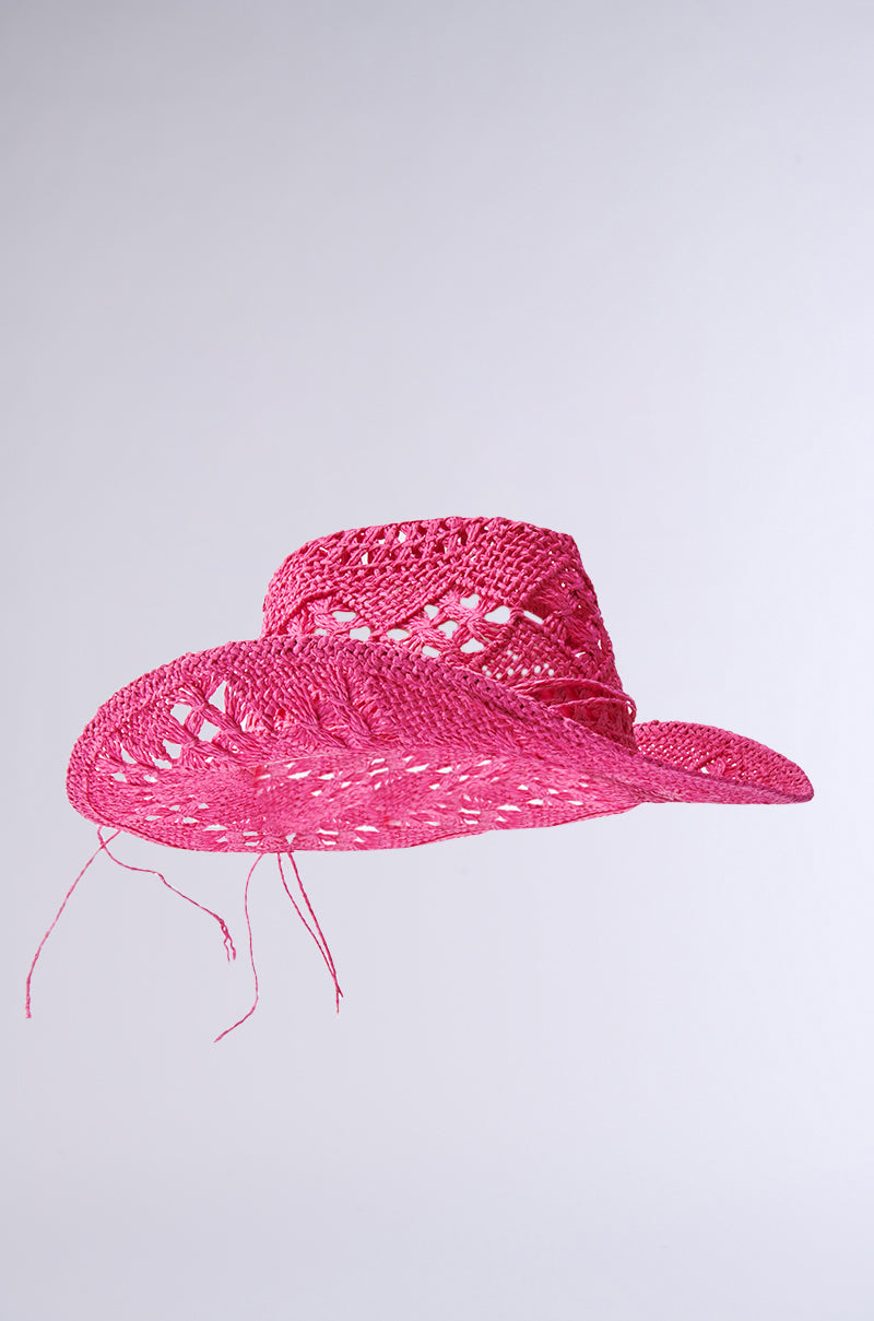 The RIDE EM STRAW COWBOY HAT, in pink, radiates cowgirl energy with its wide brim and loose strands along the edges, set against a simple gray background.